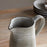 Gray ceramic pitcher on a wooden surface with stacked plates in the background